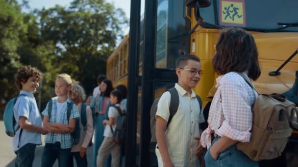 小学生在等校车 不同的学生站在黄色的穿梭机前谈话 快乐的学童在一起聊天 青少年课后在室外交流 — 图库视频影像