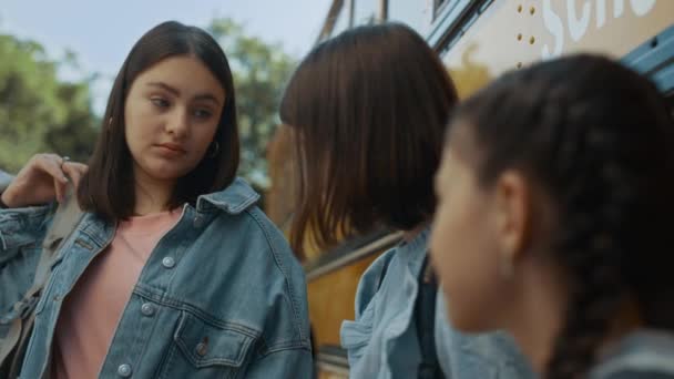 可爱的小学女生把有趣的故事告诉了与青少年亲密的朋友 快乐的学生和同学们一起站在黄色的校车旁 放学后聊天的少女 — 图库视频影像