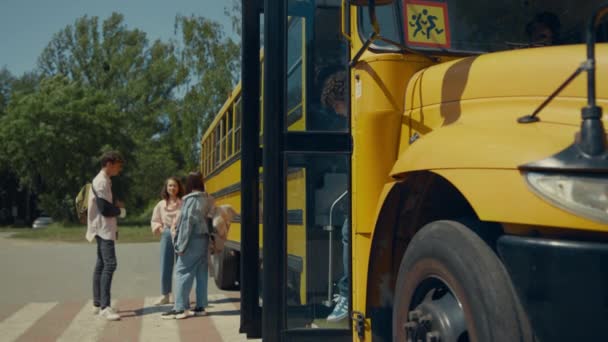 两个学生出去乘校车 兴高采烈的青少年站在校车旁聊天 三个朋友摆姿势在阳光下聊天 男生背着背包离开了黄色的穿梭车 学习概念 — 图库视频影像