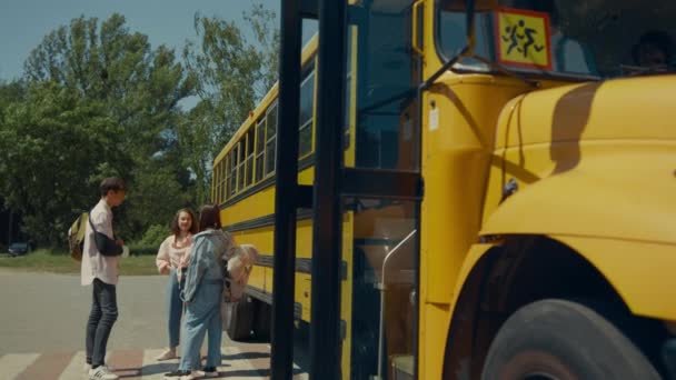 两名十多岁的同学开着黄色校车离开了学校 重点是认真的学生走出校车 不同的快乐少年站在一起 在儿童车流旁交谈 — 图库视频影像