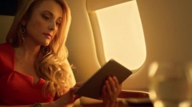 Odaklanmış CEO tablet bilgisayarı uçağın yakın planında. Patron, ortaklarla sanal görüşme ayarladı. Güzel bir iş kadını altın güneş ışığında şirket jetine biner. Profesyonel analiz sunumu