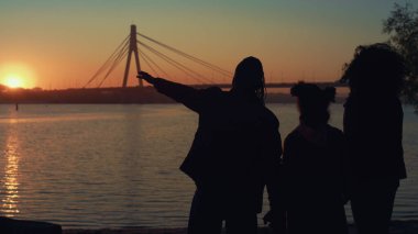 Nehir kıyısında duran rahat aile silueti. Güzel altın gün batımı zamanı. Kimliği belirsiz ebeveynler el ele tutuşup geceyi birlikte geçirmekten hoşlanırlar. Duygusal bağ tasasız çocukluk kavramı.