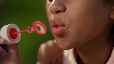 Tatlı çocuk sabun renkli baloncuk portresi üflüyor. Tasasız çocukluk kavramı. Gülümseyen Afrikalı Amerikalı kıvırcık kız parkta eğleniyor. Sevimli kız hafta sonunun keyfini çıkar.