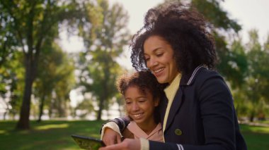 Neşeli anne park portresinde selfie çekiyor. Anne çocuk arasında nazik bir ilişki. Çekici Afrikalı Amerikalı kadın gülümseyen kız çocuğuna sarılıyor. Duygusal bağ tasasız çocukluk.