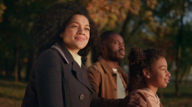 Sonbahar parkında gün batımını izleyen bir çift çocuk portresi. Boş zaman bahçesi. Çekici Afro-Amerikan annesi, rüya gibi kızıyla konuşarak sıcak güneş ışığının tadını çıkarıyor. Aile bağı rahatlatıcı.
