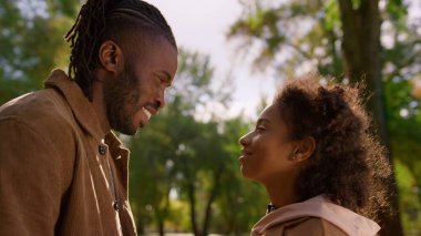 Gülümseyen baba sonbahar parkında kızına dokunuyor. Birbirine değer veren insanlar. Yakışıklı Afrikalı Amerikalı adam mutlu baba koşulsuz sevgisini ifade ediyor. Sevgili aile şehir bahçesinde dinleniyor..