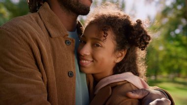 Fotoğraf makinesi görünümlü Afrikalı Amerikalı kız. Bilinmeyen baba çocuğu kollarına aldı. Neşeli, rahat kız Peder Sunny Park 'la eğleniyor. Mutlu kıvırcık saçlı çocuk anne babasıyla birlikte dinleniyor..