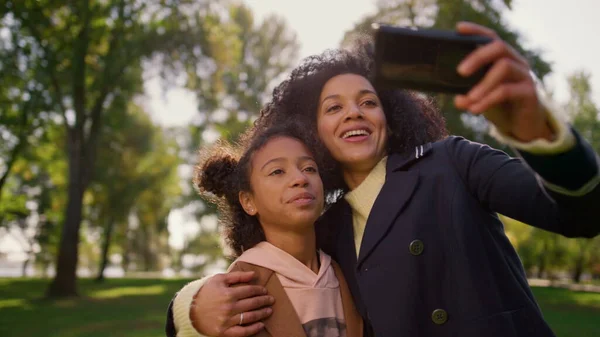 Joyful family making selfie video social media account. Celebrating mother day. Attractive african american woman holding smartphone embracing smiling daughter. Emotional connection between child mom