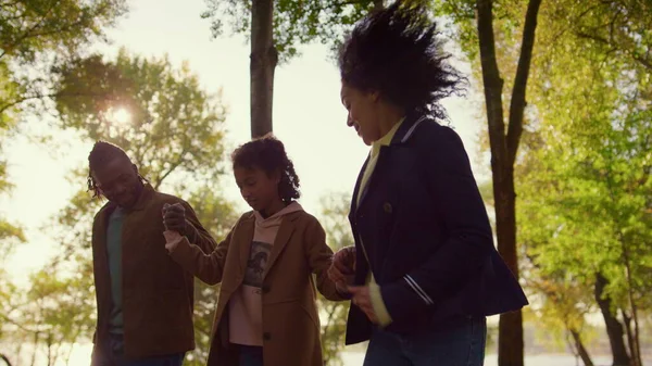 Ebeveynler, çocuğun sonbahar parkında el ele tutuşmasına yardım ediyor. Gülümseyen Afro-Amerikan baba kıvırcık anne kızını dışarıda cesaretlendiriyor. Neşeli aile eğlence zamanı konsepti.