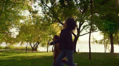 Mutlu aile çocuğu, güz şehri bahçesinde el ele tutuşarak yürüyor. Neşeli Afro-Amerikalı kadın, kızıyla birlikte parktan atlama yarışına katılıyor. Sevgi dolu aile dışarıda dinleniyor..