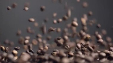 Kahve çekirdekleri yakından düşer. Kavrulmuş kahve çekirdekleri masaya düşüp zıplıyor. Aromatik taze taneler masaya dökülüyor. Karanlık arka planda enerjik içecekler için kafein hasadı manzarası. 