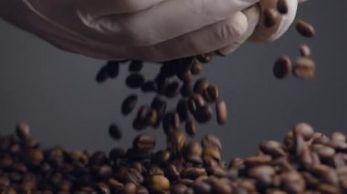 Elleri taze kahve tanelerini yakından tutuyor. Kahverengi aromatik tohumlar yığının üzerine dökülüyor. Kimliği belirsiz kişi beyaz eldiven giyip avuç içlerine kafein alıyor. Kaliteli kahve çekirdeklerini kontrol ediyorum..