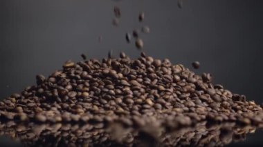 Kahve çekirdekleri üstteki yığının üzerine dökülüyor. Kavrulmuş kafein taneleri karanlık zemine düşüyor. Kahverengi aromalı kahve çekirdekleri. Enerjik bir sabah içeceği için mükemmel malzeme..