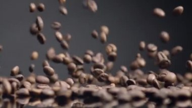 Organik kahve çekirdekleri arka fona düşüyor. Güzel kavrulmuş kahve taneleri arka planda. Aromatik taze kafein tohumları yüzeye dökülüyor. Enerjik sabah içeceği için doğal mahsul.