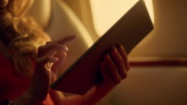Uçak yolculuğunda el taraması tablet bilgisayarı yakın plan. Yolcu jette dinleniyor. Tanınmayan zarif bir kadın, elinde ped ekrandan alışveriş yapıyor. Pencere deliğindeki aygıtı kullanarak bilinmeyen ceo çalışıyor.