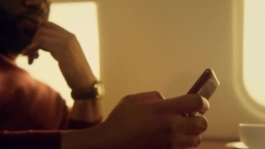 Odaklanmış adam uçak penceresinde akıllı telefona bakıyor. El ele tutuşan cep telefonu. Ciddi bir CEO borsa verilerini kontrol ediyor. Endişeli, Afro-Amerikan internet ağı. Erkek profesyonel konsept