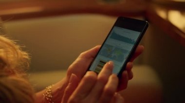 Cep telefonunun yakın planında veri tablosu tutan eller. Bilinmeyen yönetici gezide çalışıyor. Tanımlanamayan orta yaşlı kadın CEO ekrana dokunarak iş ölçümlerini kontrol ediyor. Akıllı telefon kullanan başarılı bir iş kadını