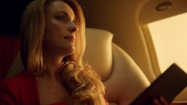 Ticari jet gezisinde tablet üzerinde çalışan zarif bir yönetici. Eller pedleri yakın tutsun. Çekici zengin iş kadını pencerede ekran tarayıcı ağına dokunuyor. Düşünceli kadın sosyal medya hesaplarını kontrol ediyor