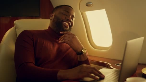 快乐的家伙在网上检查报告 在飞机上的窗口关闭时做了一个肯定的手势 笑着带胡子的商人工作笔记本电脑得到了好消息 富有的非洲裔美国人商务旅行完成项目 — 图库视频影像
