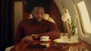 Mutlu adam birinci sınıf yakın plan uçuyor. Gülümseyen yolcu uçak penceresi. Yakışıklı Afro-Amerikan iş adamı lüks jetle şirket gezisinin tadını çıkarıyor. Zengin beyefendi iş seyahatinde dinleniyor..