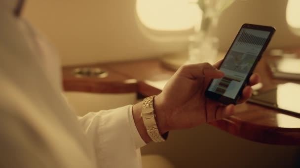 出張先でスマートフォンのチャートを見ているマネージャー 高級キャビンで携帯電話を手を閉じてください 知られていないアラビア語のマネージャーCeoは飛行機の販売統計を分析している ビジネス技術の概念 — ストック動画