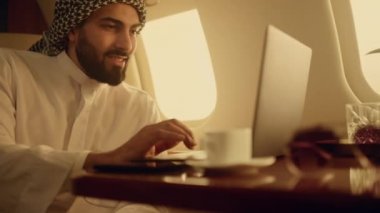 Neşeli iş adamı internette geziniyor. Yakın plan dizüstü bilgisayarda klavye. Gülümseyen sakallı Arap sörf internette iş seyahatinde sohbet ediyor. Başarılı bir adam lüks bir uçakta dinleniyor..