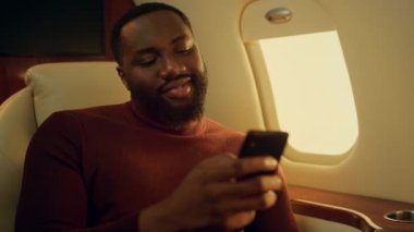 Uçak yolculuğunda internette sohbet eden olumlu bir adam. Akıllı telefonu yakından tutan eller. Mutlu Afro-Amerikan yolcular iş seyahatlerinde uygulama iletişimiyle eğleniyor. Mesajları okuyan mutlu bir adam..