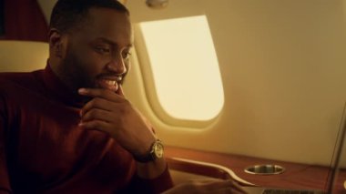 İş seyahatinde klavye yazan neşeli bir adam. Afrika kökenli Amerikalı sosyal medyadaki arkadaşına mesaj atıyor. Gülümseyen sakallı adam uçak vitrinine e-posta yolluyor. Başarılı CEO konsepti