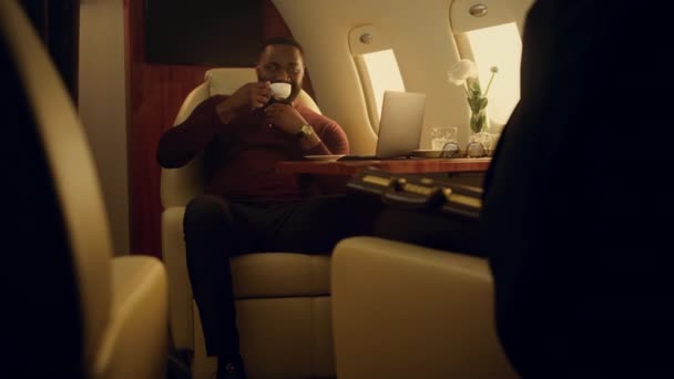 成功したビジネスマンは飛行機の窓でオンラインで閲覧する ビジネス旅行の仕事のラップトップコンピュータを入力することを中心に アフリカ系アメリカ人の男性がソーシャルメディアでコーヒーを飲む 飛行機旅客コンセプト — ストック動画