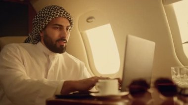 İş seyahatinde bilgisayarın yakın planda olduğu doğrulandı. Gülümseyen Arap çevrimiçi sohbetten zevk alıyor. Başarılı bir iş adamı, Müslüman kıyafetiyle e-posta yazan bir iş adamı. İş eğlencesi konsepti.