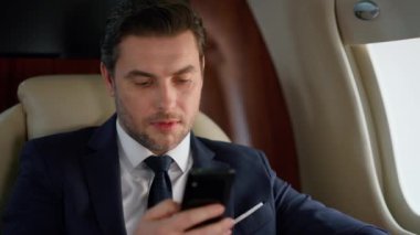 Uçakta yakın plan akıllı telefon kullanan yakışıklı bir girişimci. Başarılı seyahat CEO 'su takım elbise içinde birinci sınıf. Odaklanmış zarif adam e-postayı kontrol ediyor. Ciddi bir yönetici borsayı analiz ediyor..