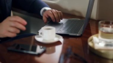 Yakın çekim el bilgisayarı uçak gezisinde online video konferansına başlıyor. İşletme sınıfında tanınmayan başarılı bir adamın el sallaması. İş adamı kahve fincanı alıp uçakta çalışıyor.