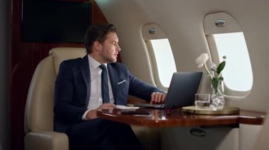 Şirket gezisinde odaklanmış iş adamı görünümlü bilgisayar. Zengin adam dizüstü bilgisayarda çalışıyor. İnternet iş raporlarını kontrol ediyor. Başarılı yönetici uçak penceresinde sunum oluşturdu. Erkek profesyonel konsept.