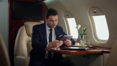 Gergin yönetici lüks jette tablet bilgisayar tutuyor. Odaklanmış adam görünümlü Ped-screen şirket raporları. Şaşırmış başarılı iş adamı dijital bilgisayara dokundu. Uçakta Ceo çözme sorunu
