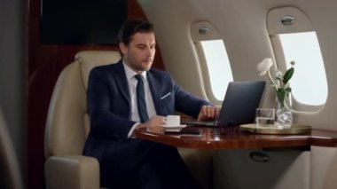 Uçakta çalışan stresli bir profesyonel bilgisayar. İşletme sınıfında kahvesini yudumlayan odaklanmış bir adam. Profesyonel görünümlü bilgisayar ekranı daktilo ağı. Hayal kırıklığına uğramış CEO çevrimiçi raporları kontrol ediyor