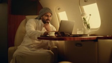 Gülümseyen iş adamı uçakta klavye çalıyor. Neşeli adam iş gezisinde internette sohbet ediyor. Müslüman kıyafetleriyle internette gezinen yakışıklı bir Arap bilgisayar. Rahatlamış müdür uçuşun tadını çıkarıyor