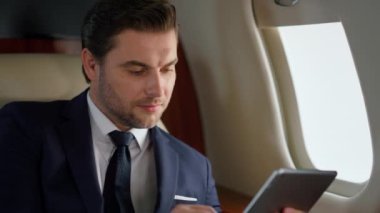 Havalı yönetici yakın planda ped bilgisayar kullanıyor. Gülümseyen adam birinci sınıfta uçuyor. Başarılı girişimci dijital bilgisayar tarama ağını araklıyor. CEO 'nun pencerede veri kontrolü yaptığını düşünüyorum.