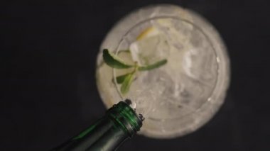 Buzlu limonlu naneli kokteyl yakın plan. Buzlu nane ve limonlu şişeden yavaş çekimde soda dökülüyor. Kıvırcık yaz içkisi siyahın üstünde. Kokteyl süreci konsepti yapılıyor
