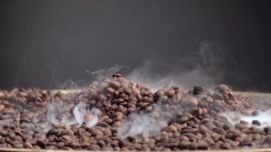 Kavrulmuş kahve çekirdekleri yakından pişiyor. Hafif duman, koyu arkaplanda ağır çekimde taze kahverengi aromatik tohumlardan geliyor. Kokulu kahve taneleri enerjik bir sabah içeceği için kızarıyor.. 
