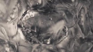 Buz küpleri köpüren su yavaş çekimde dönüyor. Hava damlaları buzla kaplı, soda bardağı köpüklü suyla. Kabarcıklar yüzey makro üst görünümünde patladı. Saf meşrubat konseptini tazeliyorum.