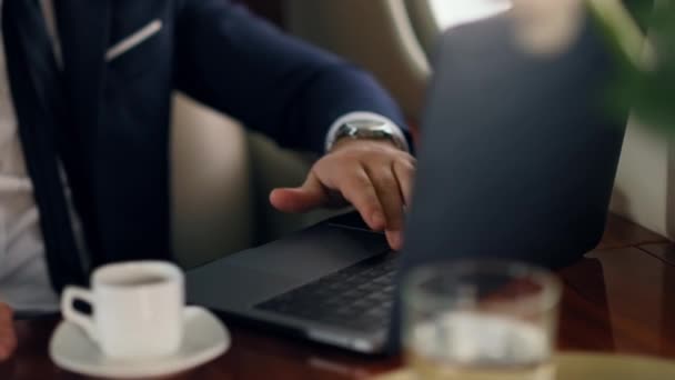 ビジネスジェットでオンライン通話を開始する男 企業旅行でビジネスマンの手を振ってノートパソコンのドリンクコーヒーを手を閉じます リラックスした未知のマネージャーの投資家は 仮想会議について話します 裕福なライフスタイルの概念 — ストック動画