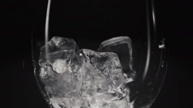 Donmuş bloklar düşen şarap kadehleri yavaş çekimde yakınlaşır. Buz kırılan küplerin içine şeffaf cam dökülüyor. Soğuk içecekler ve kokteyller makro siyah arka plan. Susuzluk giderici konsept