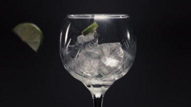 Limonlar nane şekeri, buz küpleri, şarap kadehleri, yakın plan. Donmuş nane şekeri ve limonlar şeffaf camın içinden yavaş çekimde atılıyor. Makro siyah arkaplan kuruluyor. Ev yapımı içki konsepti