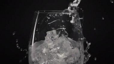 Soğuk buz küpleri yakın plan cam içerler. Şeffaf şarap kadehinden akan temiz su yavaş çekim tespiti yapıyor. Köpüklü su siyah arka plan dökülüyor. Taze soda kokteyli.
