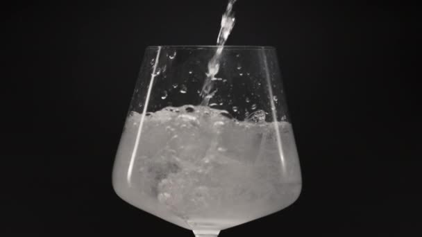 飞溅的水倒入冰杯 使冰杯的运动缓慢 在干净的玻璃杯中加入冰块的气泡液体 空气滴在矿泉水中移动 玻璃窗黑色背景 有机鸡尾酒概念 — 图库视频影像