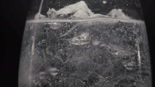 冰冻块闪烁着酒杯特写 松软起泡的纯苏打水在温格拉斯慢动作 碳化矿泉水形成黑色背景 更新鸡尾酒概念 — 图库视频影像