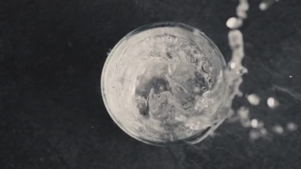 泡状の氷の水のガラスの上からの眺め ゆっくりとした動きで透明なカップで固定ソーダミネラルドリンク 炭酸水で満たされた容器 暗い背景のマクロ 夏の爽やかな飲み物のコンセプト — ストック動画