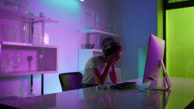 Competitive gamer playing esport computer game at neon lights home closeup. Emotional beautiful girl losing virtual battle in headset on weekend night. Upset woman looking screen check round results.
