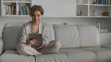 Öğrenci oturma odasında çevrimiçi video konuşması yapıyor. Koltukta çalışırken ped kullanan gülümseyen kız. Mutlu kadın, yeni evimizin içini nöbetçi olarak gösteriyor. Çekici bayan taşındıktan sonra evinde dinleniyor.