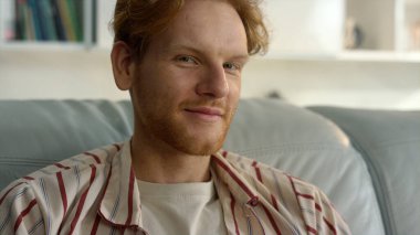 Mutlu hipster dinlenme koltuğu evde yakın çekim. Gülen kızıl adam kanepeye uzan. Neşeli sakallı serbest çalışan uzak bir iş yerinde işten sonra dinleniyor. Tatmin olmuş genç baba, sakin atmosferin tadını çıkar.